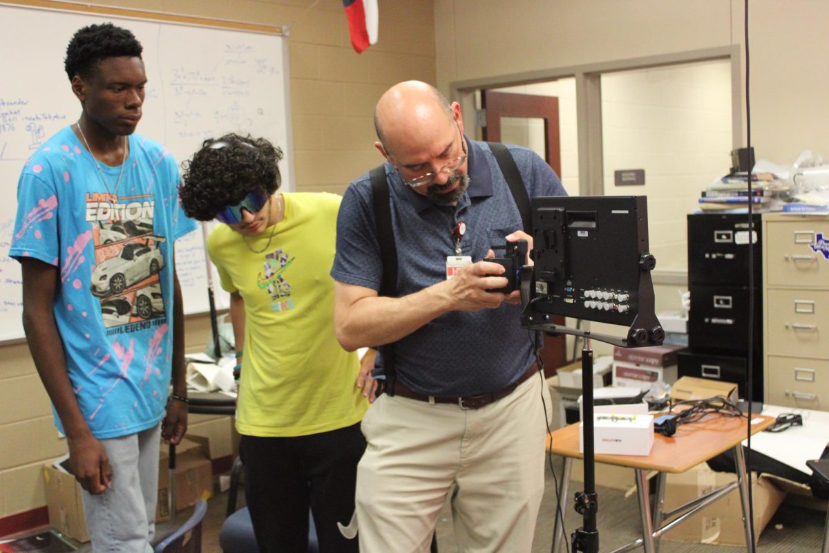 Senior Gamarion James and sophomore Christopher Pineda observe the task of setting up the Panasonic AG-UX 180 camcorder, as Mr. Bourbois instructs how to put the pieces together.