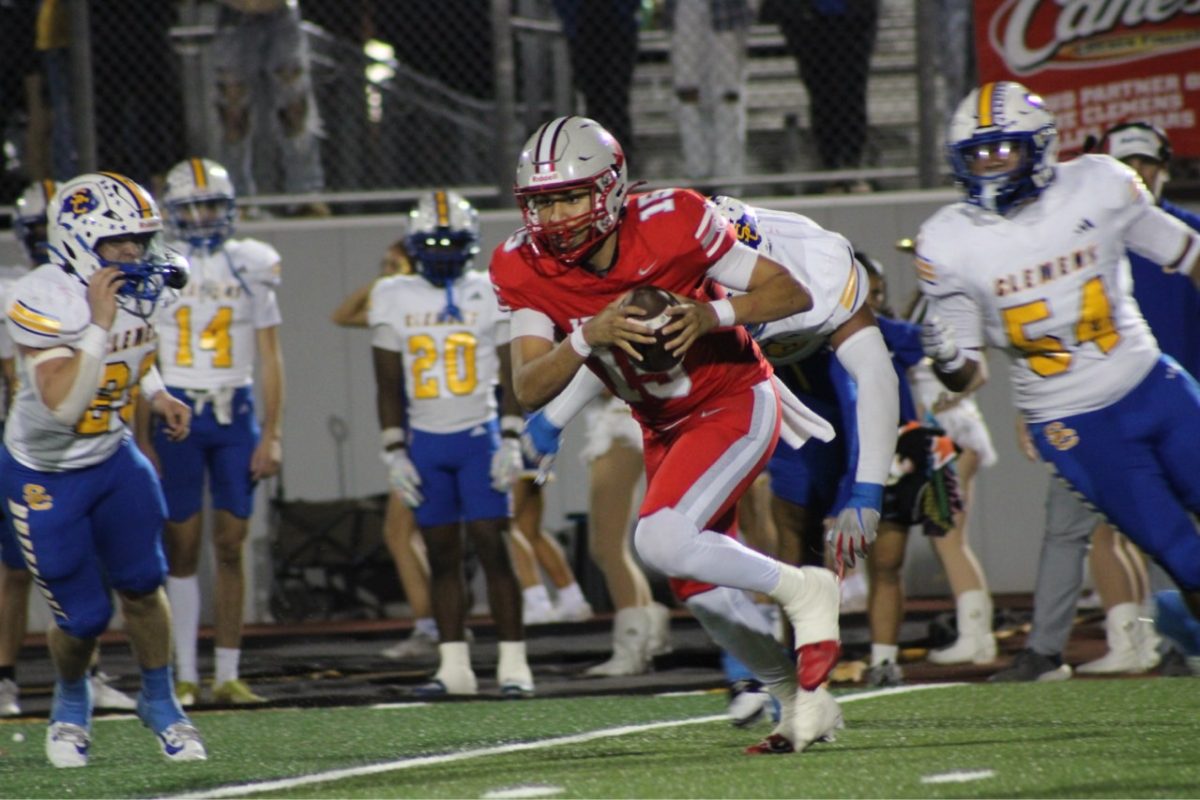 #15, quarterback Elijah Favela, holds the ball while rushing past multiple Clemens athletes.